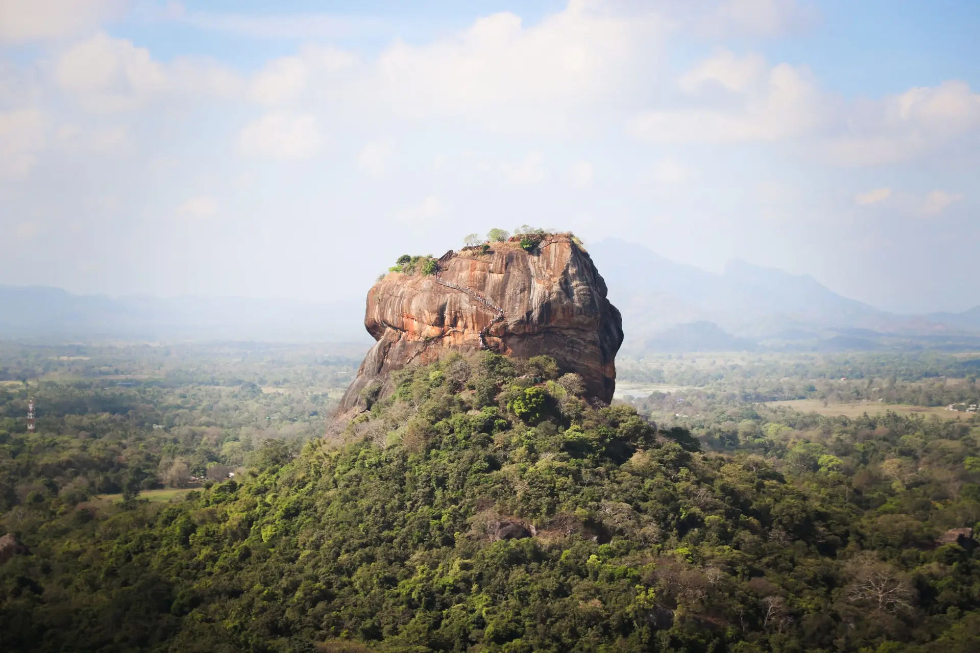 View of the iconic Sigiriya Rock Fortress, surrounded by lush vegetation in Sri Lanka.